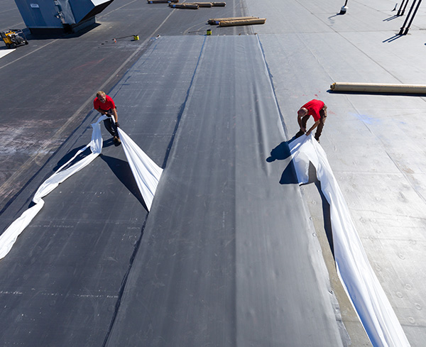 Two roofers laying down RubberGard EPDM on a rooftop